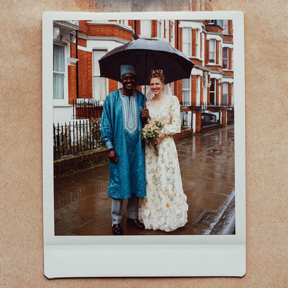 An instant photograph of a bride and groom under an umbrella on a rainy terraced street