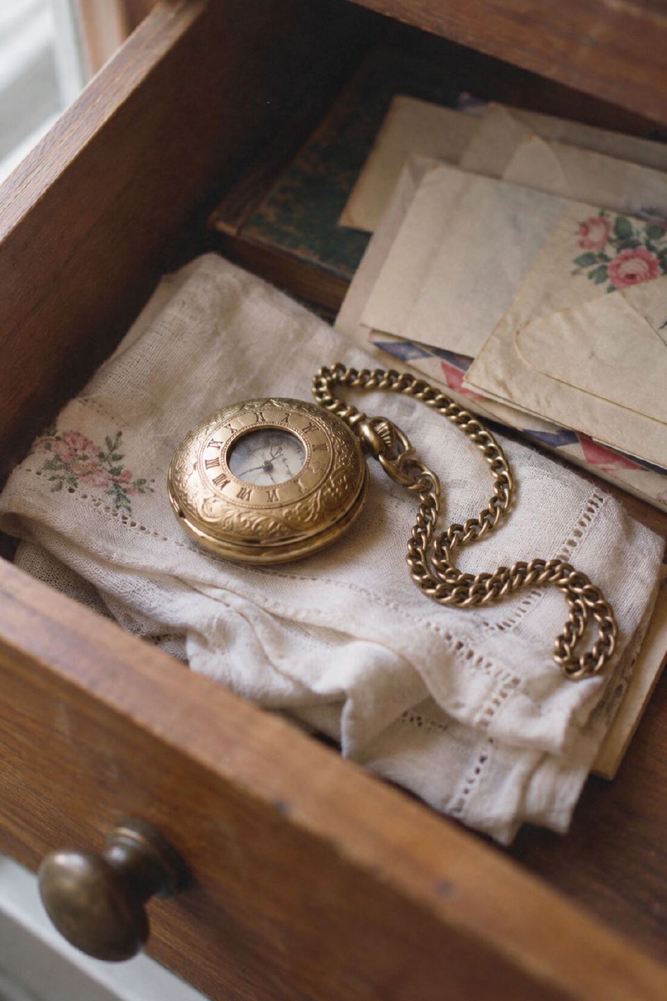 A gold pocket watch and chain resting on folded linen in an open drawer of old letters